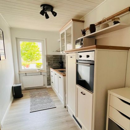 Eine moderne Küche mit weißen Möbeln und Holzdetails. Das Fenster bietet einen Blick auf grünes Laub.