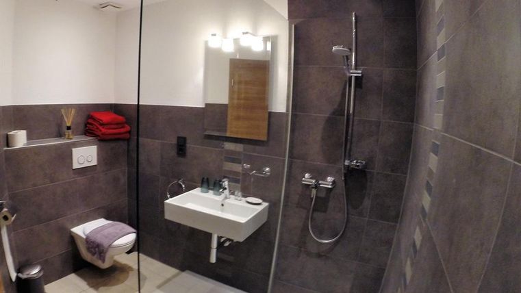 Ein modernes Badezimmer mit dunklen Fliesen und einer großen Dusche. Es gibt ein Waschbecken, eine Toilette und gestapelte rote Handtücher.