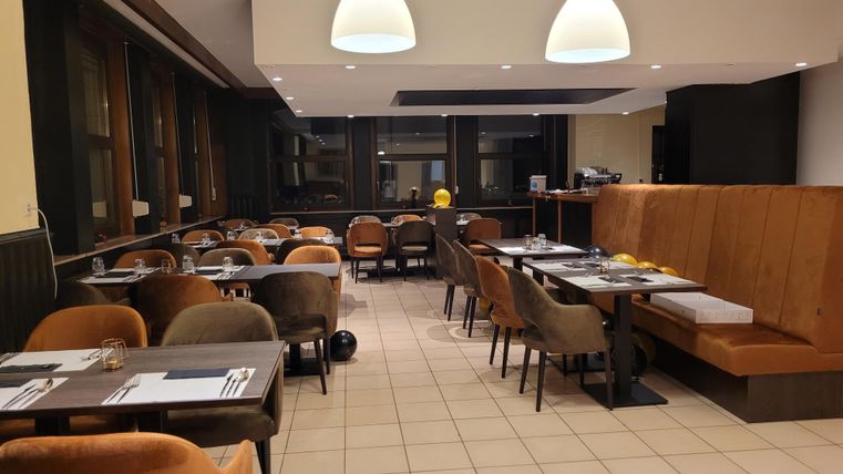 Ein modernes Restaurant mit gemütlichen Stühlen und Tischen. Die Beleuchtung ist freundlich und sorgt für eine einladende Atmosphäre.