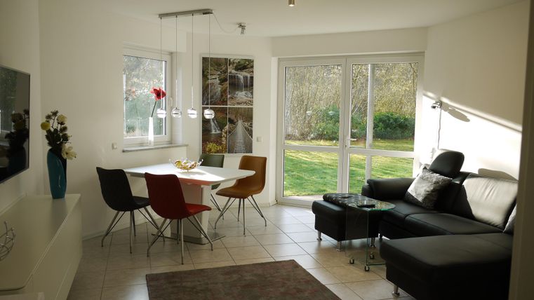 Eine helle Wohnräume mit einem modernen Sofa und einem Esstisch. Große Fenster bieten Blick auf den Garten.