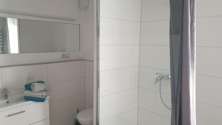 Ein modernes Badezimmer mit einer Glasdusche und einem weißen Waschbecken. Frische Handtücher liegen bereit und ein Spiegel reflektiert den Raum.
