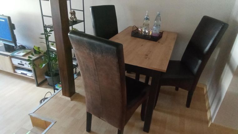 Ein kleiner Essbereich mit einem Holztisch und vier Stühlen. Auf dem Tisch stehen zwei Wasserkaraffen.