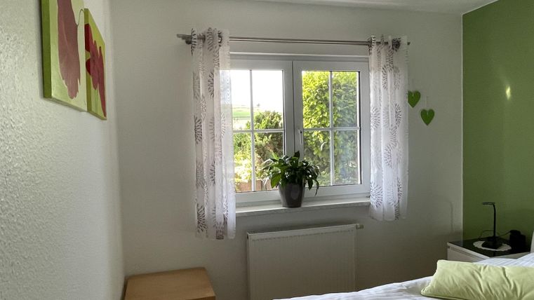 Ein gemütliches Schlafzimmer mit einem Fenster und vielen Pflanzen. Die Wände sind in sanften Farben gestrichen, und es gibt ein Bett mit hellen Kissen.