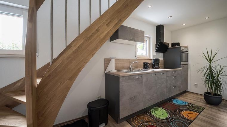 Eine moderne Küche mit einer Holztreppe und buntem Teppich. Helle Wände und eine Pflanze sorgen für eine freundliche Atmosphäre.