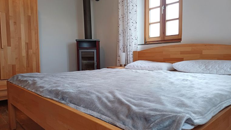 Ein gemütliches Schlafzimmer mit einem großen Bett und einem Holzofen. Die Fenster lassen viel Tageslicht herein und sorgen für eine einladende Atmosphäre.