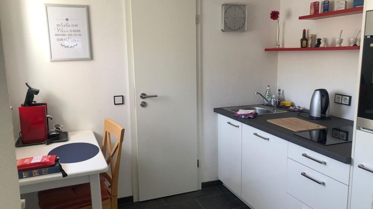 Eine moderne Küche mit weißen Schränken und schwarzen Arbeitsflächen. Es gibt einen kleinen Tisch mit Stühlen und einige Kochutensilien auf den Regalen.