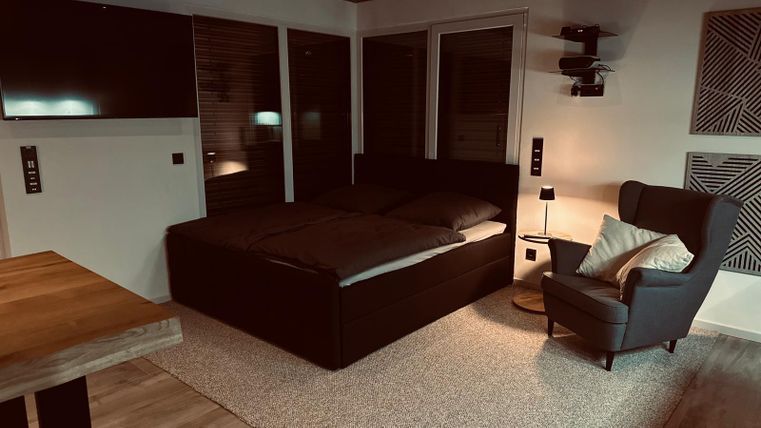 Ein gemütliches Schlafzimmer mit einem großen Bett und einem bequemen Sessel. Die Atmosphäre ist warm und einladend, mit sanfter Beleuchtung.