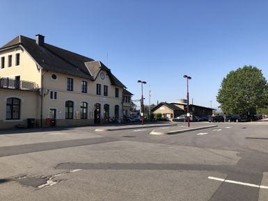 Ein Bahnhof mit schöner Architektur und einem klaren blauen Himmel. Auf der Straße sind einige Bäume und Straßenlaternen zu sehen.
