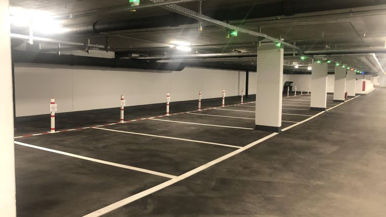 Ein leerer Parkhaus mit mehreren Parkplätzen. Die Beleuchtung ist hell und es gibt weiße Markierungen und Verkehrsleitpfosten.