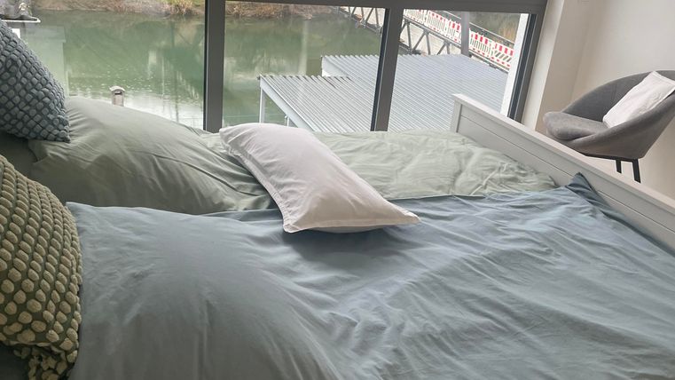 Ein modernes Schlafzimmer mit einem großen Fenster und mit einem wunderschönen Blick in die Natur. Bettwäsche ist vorhanden.