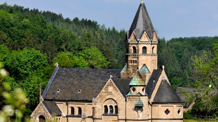 Kirche in Mirbach umgeben von grünen Bäumen und blauem Himmel.