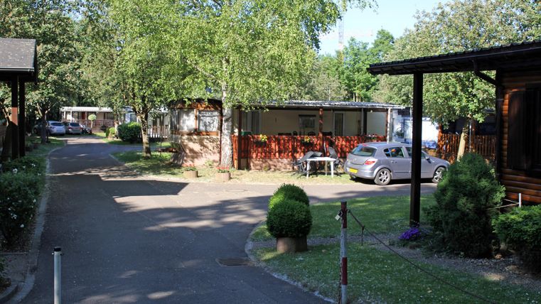 Ein ruhiger Ferienplatz mit Bungalows und einem grünen Bereich. Die Sonne scheint auf die gepflegte Umgebung und das Auto parkt am Straßenrand.