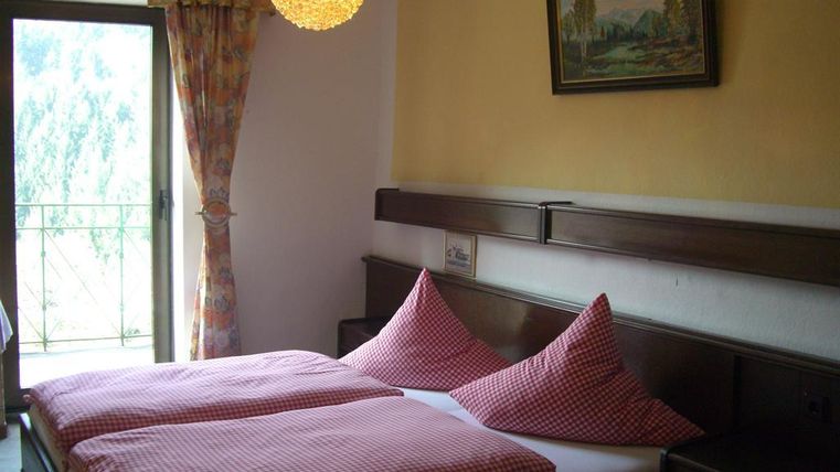 Ein gemütliches Schlafzimmer mit zwei Einzelbetten und karierten Kopfkissen. Ein Fenster mit Zugang zu einem Balkon lässt Tageslicht herein.