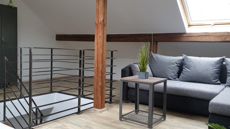 Ein modernes Wohnzimmer mit einem grauen Sofa und einem Tisch. Der Raum hat helle Wände und Holzdetails.