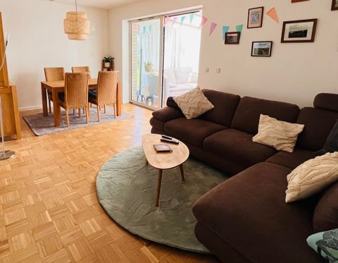 Ein gemütliches Wohnzimmer mit einem großen braunen Sofa und einem runden Tisch. Im Hintergrund befindet sich ein Essbereich mit einem Tisch und Stühlen.