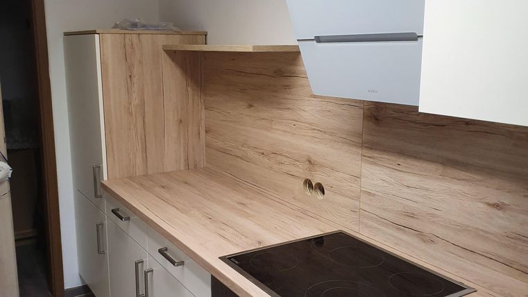 Eine moderne Küche mit Holz- und weißen Fronten. Sie verfügt über ein Kochfeld, einen Backofen und ausreichend Stauraum.