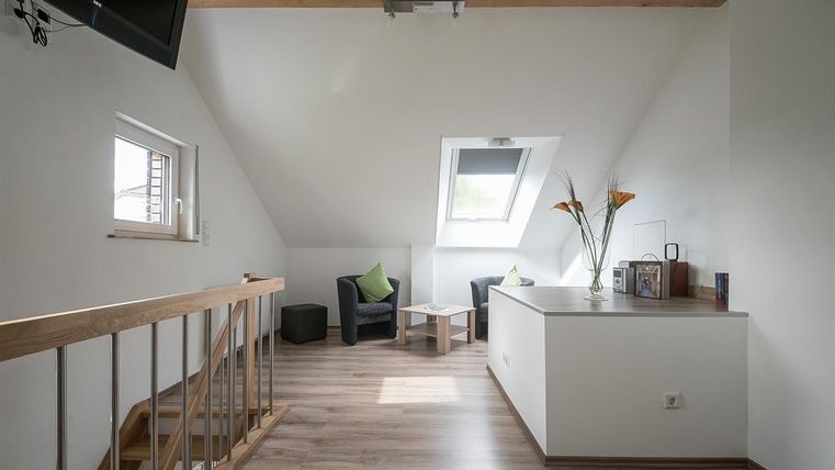 Ein heller, moderner Raum mit Dachfenstern und Holzdecke. Es gibt zwei gemütliche Sessel und einen kleinen Tisch.