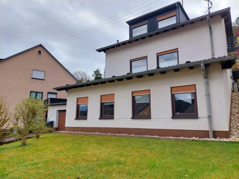 Ein modernes Haus mit mehreren Fenstern und einem Garten im Vordergrund. Es gibt auch ein benachbartes, traditionelles Gebäude.
