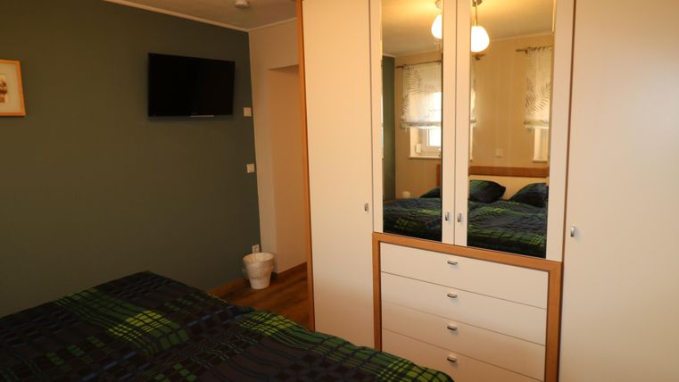 Ein gemütliches Schlafzimmer mit einem Doppelbett und einem Kleiderschrank. An der Wand befindet sich ein Fernseher und das Licht ist warm und einladend.