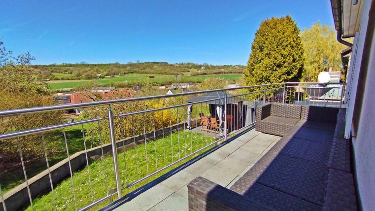 Ein schöner Balkon mit einer Aussicht auf grüne Wiesen und Bäume. Die Terrasse ist mit modernen Möbeln ausgestattet.