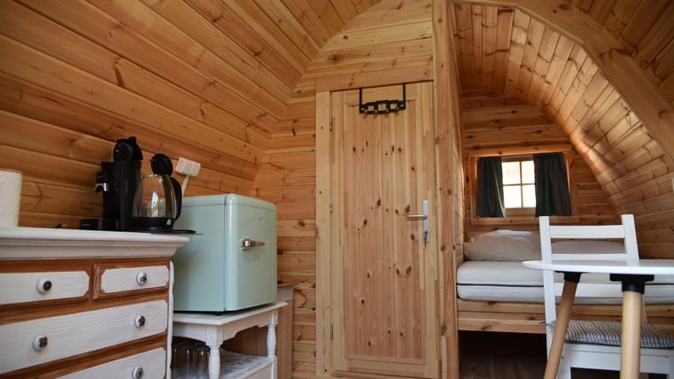 Ein gemütlicher Raum mit holzverkleideten Wänden. Er enthält eine kleine Küchenzeile, ein Bett und einen Tisch mit Stühlen.