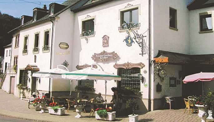 Une auberge accueillante avec une terrasse invitante et des plantes en fleurs. La façade est ornée d'éléments décoratifs.