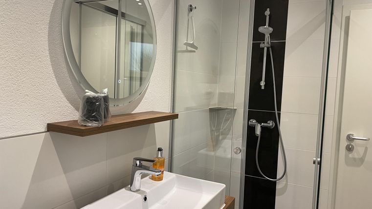 Ein modernes Badezimmer mit einer begehbaren Dusche und einem runden Spiegel. Der elegante Waschtisch ist aus Holz und Keramik.