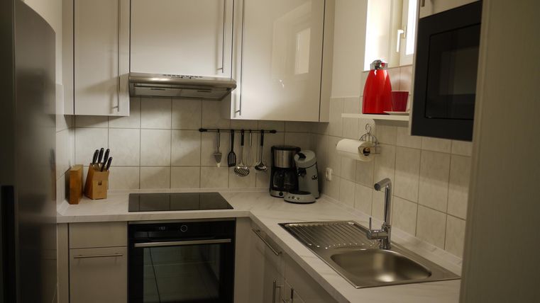 Eine moderne Küche mit weißen Möbeln und Edelstahlgeräten. Sie ist hell und gut ausgestattet mit Herd, Spüle und Küchengeräten.