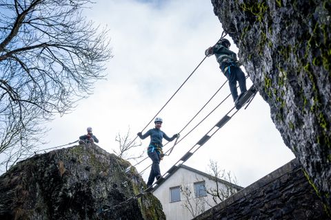 Two climbers cross a suspension bridge between two rocks.