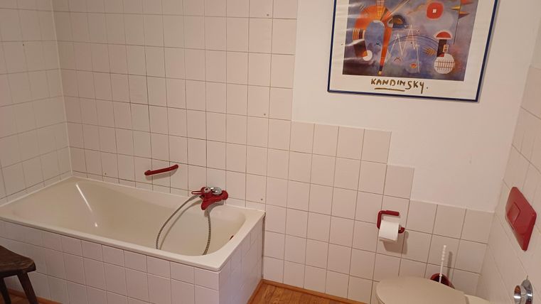 Ein einfaches Badezimmer mit einer Badewanne und einer Toilette. An der Wand hängt ein modernes Kunstwerk.