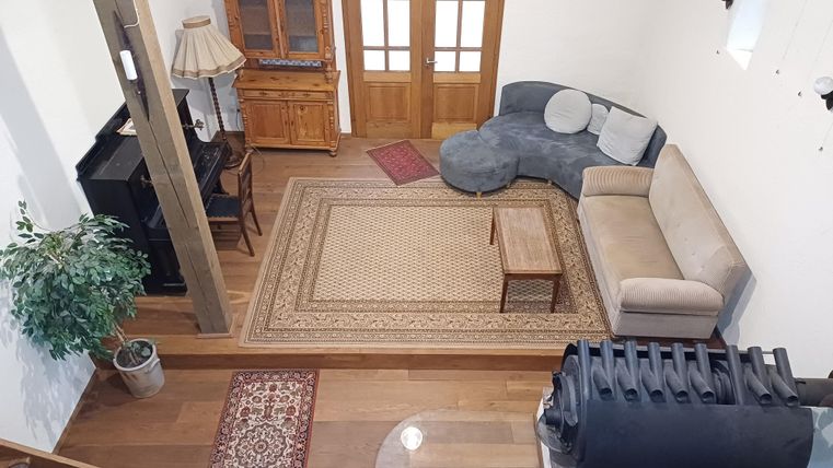 Ein gemütliches Wohnzimmer mit einem beigen Sofa und einem runden grauen Sessel. Ein Teppich und eine Holzkommode verleihen dem Raum einen warmen Charakter.