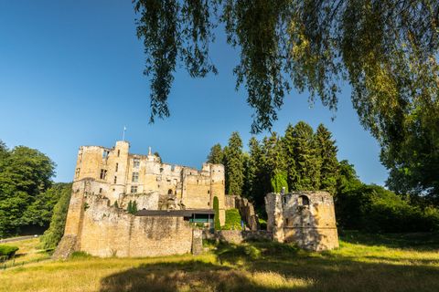 Ruine Beaufort in Luxemburg, umgeben von Bäumen und blauem Himmel.