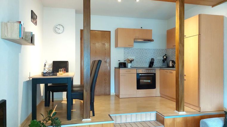 Eine moderne Küche mit Holzregalen und einer gemütlichen Essecke. Der Raum ist hell und einladend, mit klaren Linien und funktionalem Design.