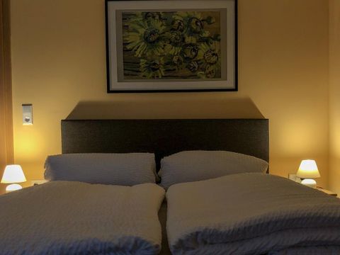 Ein gemütliches Schlafzimmer mit einem Doppelbett und weichen Kissen. Sanftes Licht von Nachttischlampen schafft eine entspannte Atmosphäre.