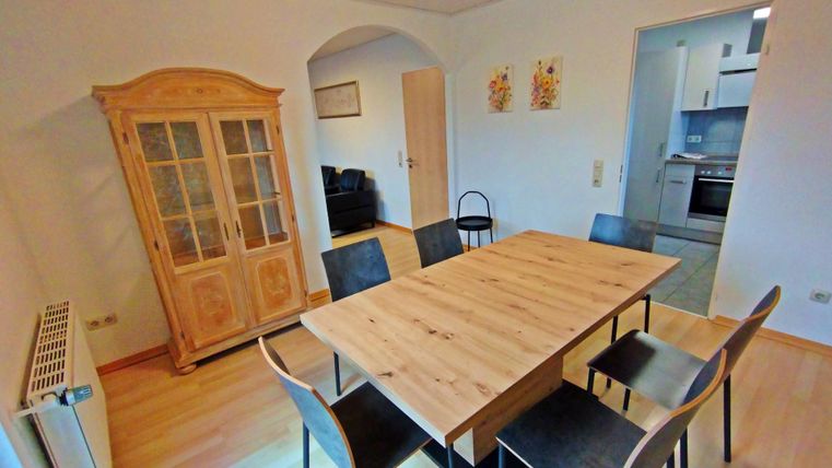 Ein gemütlicher Essbereich mit einem großen Holztisch und schwarzen Stühlen. Im Hintergrund ist ein schöner Vitrinenschrank und eine Küche sichtbar.