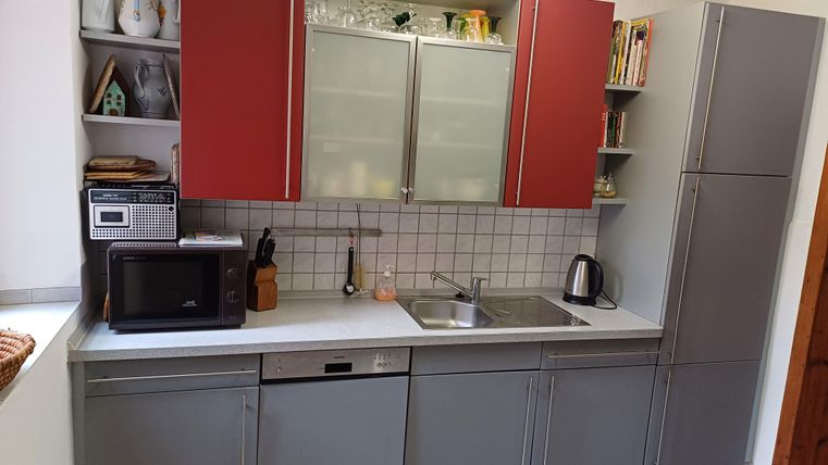 Eine moderne Küche mit grauen Möbeln und roten Schränken. Sie ist ausgestattet mit einem Waschbecken, Mikrowelle und Kühlschrank.