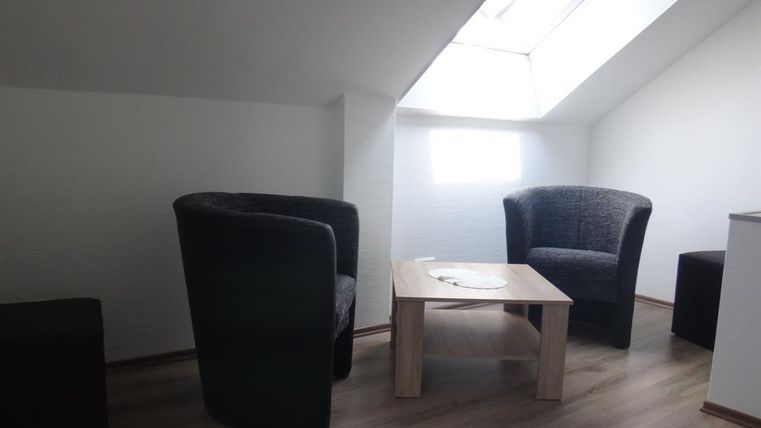 Ein gemütlicher Raum mit zwei Sesseln und einem Tisch. Es gibt ein Dachfenster, das natürliches Licht hereinlässt.