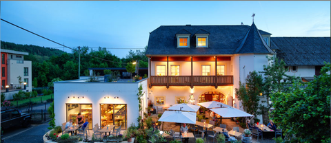 Ein Bild des Wein Restaurants Johannishof mit einem schönen Weingarten im Hintergrund. Es zeigt Speisen, Weingläser und Informationen zu Öffnungszeiten und Reservierung.