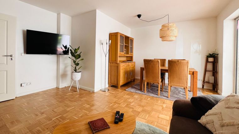 Ein heller Wohnraum mit einem gemütlichen Sofa und einem Holztisch. Der Essbereich ist mit einem Tisch und Stühlen sowie einem Fernseher ausgestattet.