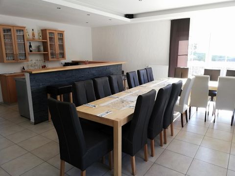 Ein modernes Esszimmer mit einem langen Tisch und bequemen Stühlen. Die große Fensterfront sorgt für viel Tageslicht und eine einladende Atmosphäre.