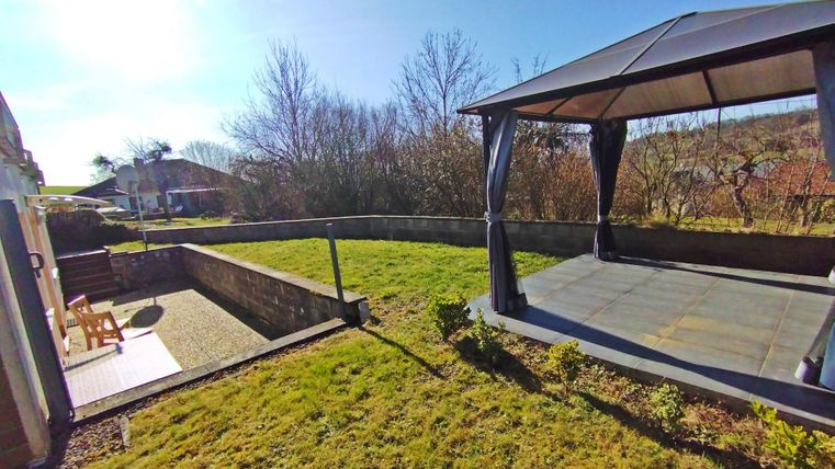 Ein schöner Garten mit einer Terrasse und einem überdachten Pavillon. Im Hintergrund sind Bäume und der klare Himmel sichtbar.