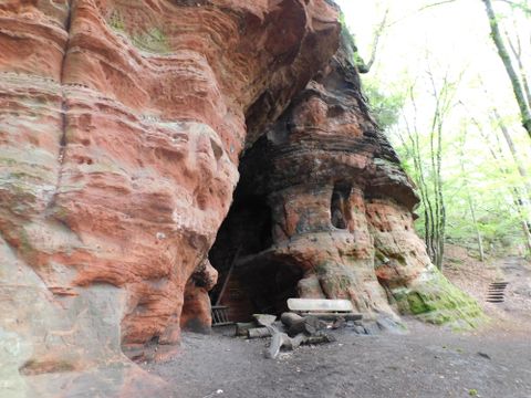 Eine beeindruckende Felsöffnung in einem Wald mit roten Sandsteinformationen. Umgeben von Bäumen, bietet der Ort eine natürliche und ruhige Atmosphäre.