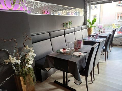Ein modernes Restaurant mit eleganten Tischdecken und dekorativen Blumen. Die Wände sind geschmückt und die Atmosphäre ist einladend.