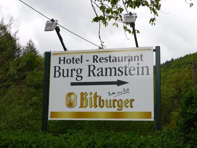 Ein Schild für das Hotel und Restaurant Burg Ramstein. Es zeigt die Richtung zur Burg und beinhaltet das Bitburger-Logo.