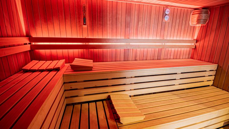 Eine moderne Sauna mit Holzbank und sanftem rotem Licht. Die Wände sind aus Holz, was eine entspannende Atmosphäre schafft.