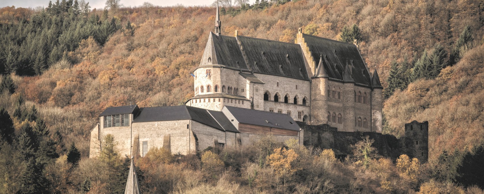 Vianden Castle sits majestically on a hill, surrounded by autumn-colored trees and a cloudy sky., &copy; Jengel
