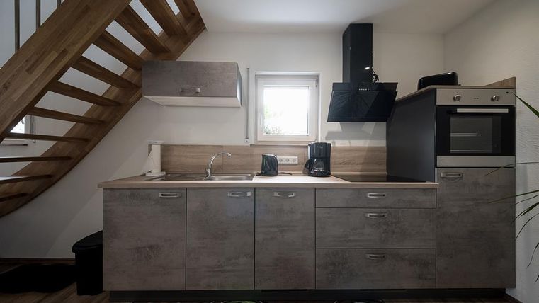 Eine moderne Küche mit Holzschränken und einem gemütlichen Treppenaufgang. Die Ausstattung umfasst eine Spüle, einen Herd und Kaffeemaschinen.