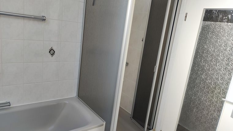 Ein modernes Badezimmer mit einer Badewanne und einer separaten Dusche. Die Wände sind in hellem Fliesenmuster gehalten.