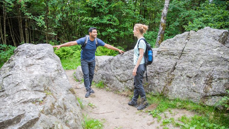 Zwei Wanderer stehen zwischen großen Felsen im Wald und unterhalten sich.