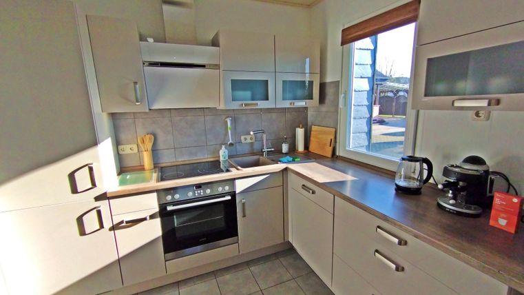 Eine moderne Küche mit hellen Schränken und einem großen Fenster. Der Raum ist gut ausgestattet mit einem Herd, einer Kaffeemaschine und anderen Kochutensilien.